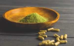 a bowl of green kratom powder next to capsules
