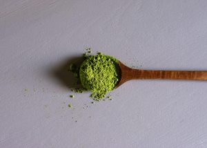 a wooden spoon filled with green kratom powder