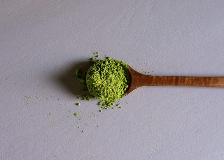a wooden spoon filled with green kratom powder