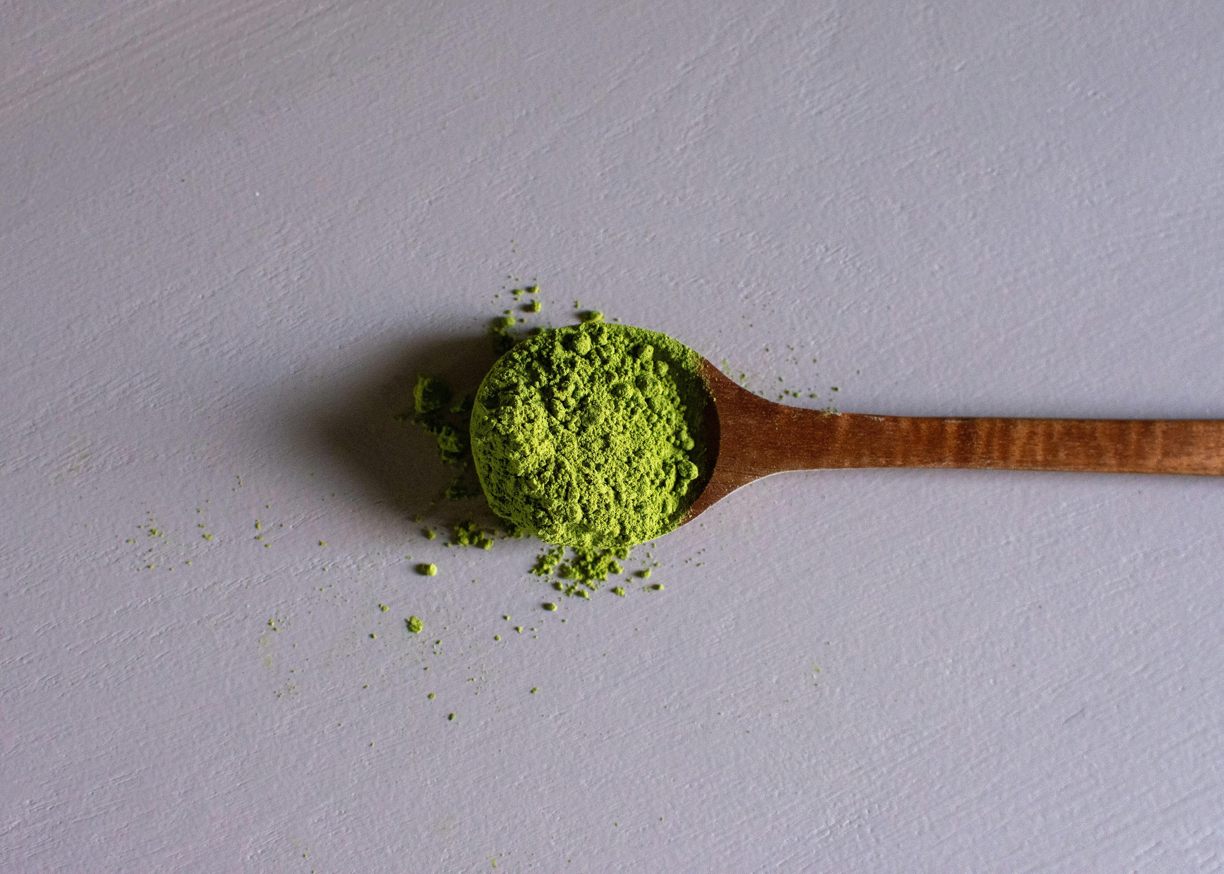 a wooden spoon filled with green kratom powder