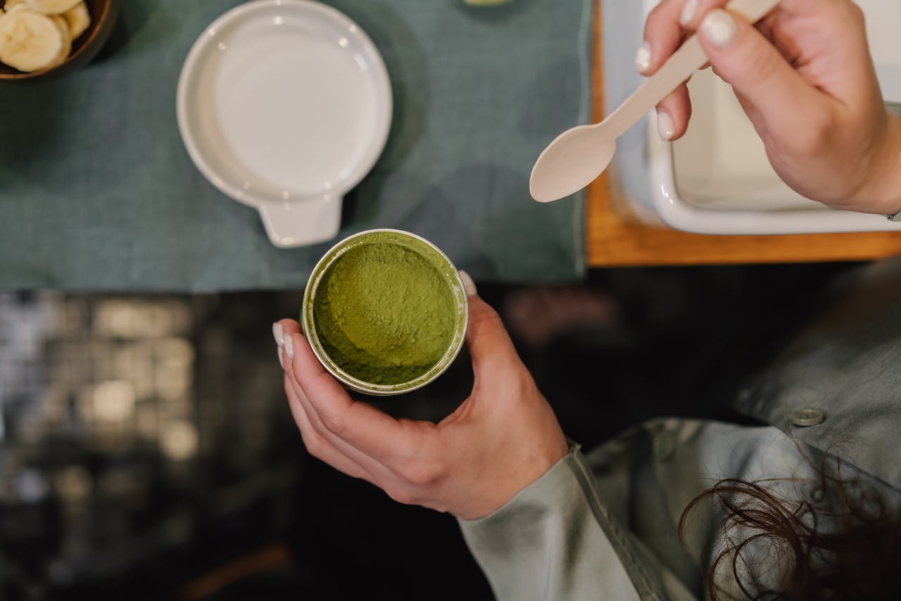 a hand holding a container with green kratom powder