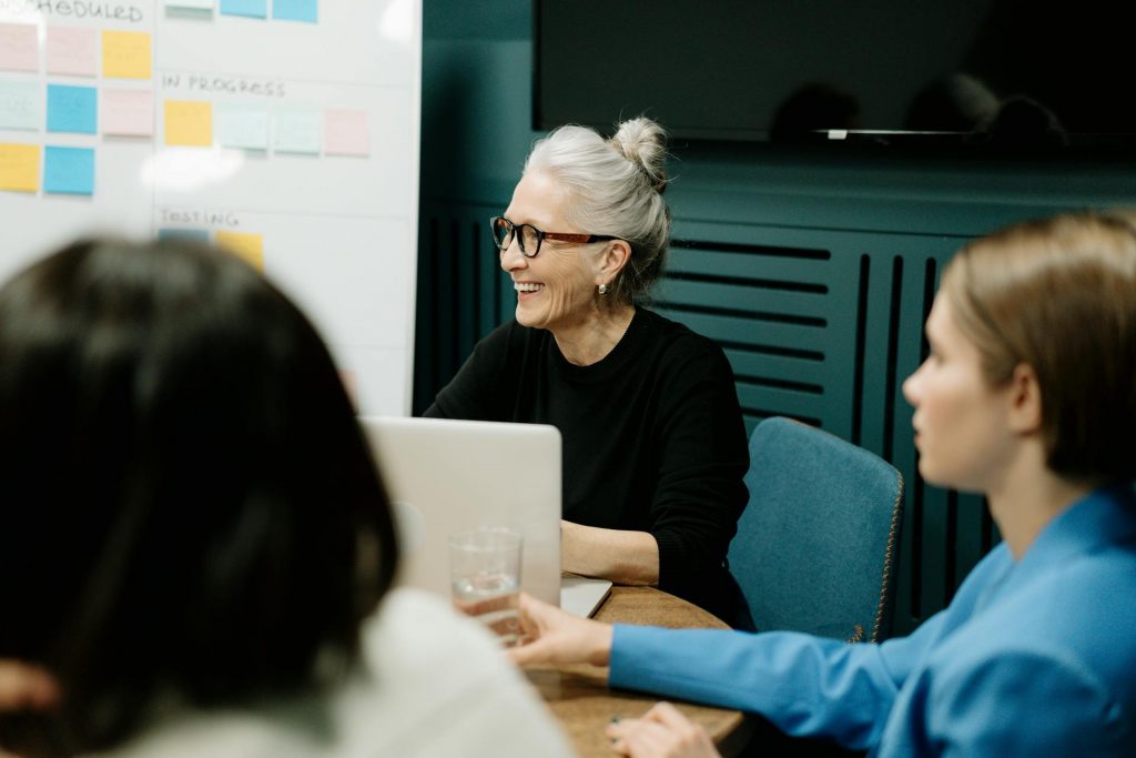 Woman in black sweater and eyeglasses sitting on chair beside woman in blue shirt